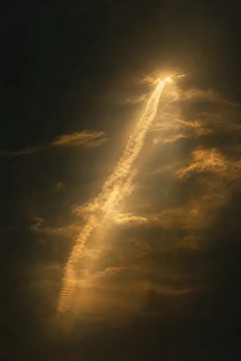 Luminous contrail trembling alone in night sky, the vanished airplane's only remaining trace