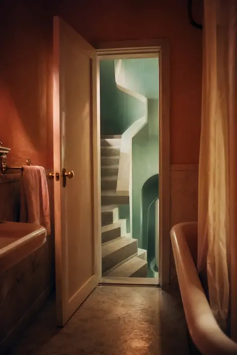 Bathroom door opens onto staircase ascending impossibly upward, pale peach walls fold into mint rooms that shouldn't connect, tilted dreamlike