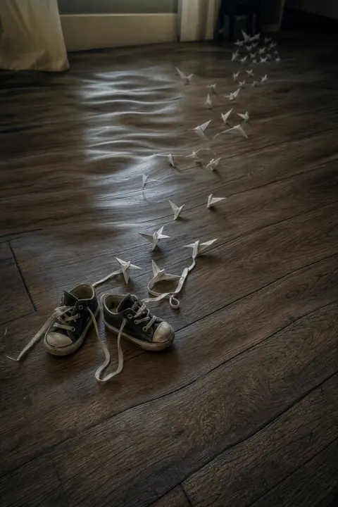 A small empty pair of shoes whose laces unravel into paper birds as the floor ripples, a dream of a dead child
