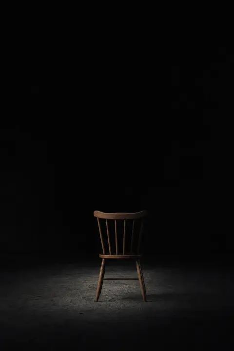 Empty chair outlined in burning gold silhouette against black void, dream symbol of marriage as dissolved presence and absence