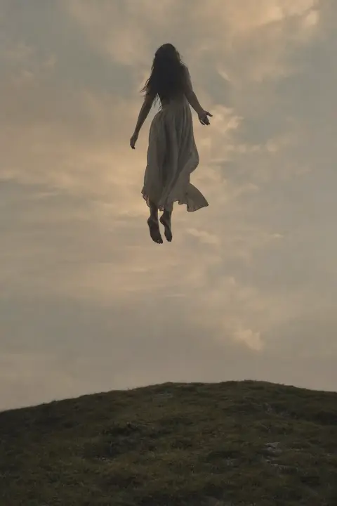Woman's silhouette floats weightlessly through amber air, hair and dress flowing downward as golden dust rises upward around her in warm dusk glow, girlfriend dream symbol