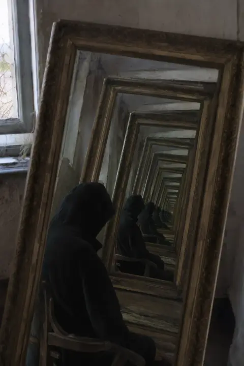 Siluetas encapuchadas se multiplican en espejos infinitos, una vela temblando en la oscuridad, reflejo de Santa Muerte